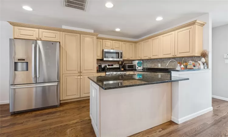 Kitchen featuring dark stone counters, dark hardwood / wood-style floors, decorative backsplash, appliances with stainless steel finishes, and a kitchen island