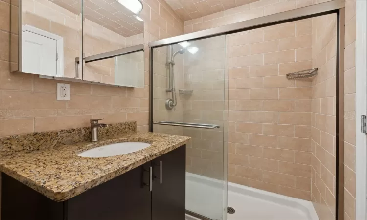 Bathroom with tasteful backsplash, vanity, a shower with door, and tile walls