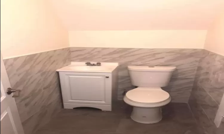 Bathroom with tile patterned flooring, vanity, toilet, and tile walls