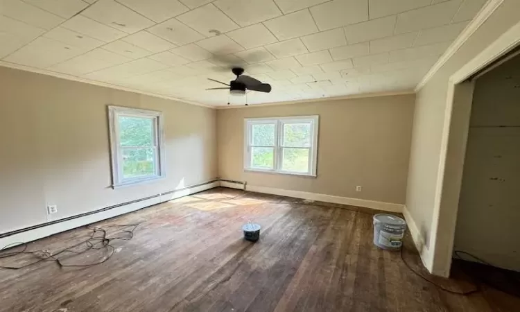 Empty room with wood-type flooring, a baseboard radiator, ceiling fan, and a healthy amount of sunlight