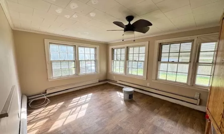 Unfurnished room featuring ceiling fan, wood-type flooring, ornamental molding, and a baseboard radiator