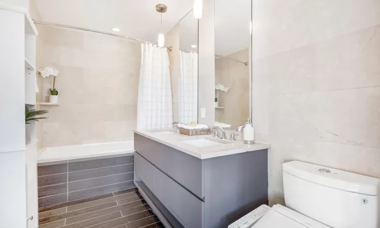 Full bathroom featuring toilet, vanity, shower / tub combo with curtain, and tile walls