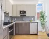 Kitchen with gray cabinetry, sink, appliances with stainless steel finishes, tasteful backsplash, and light hardwood / wood-style floors