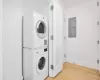 Washroom featuring stacked washer and dryer, electric panel, and light hardwood / wood-style flooring