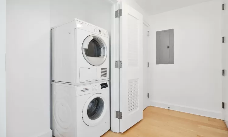 Washroom featuring stacked washer and dryer, electric panel, and light hardwood / wood-style flooring