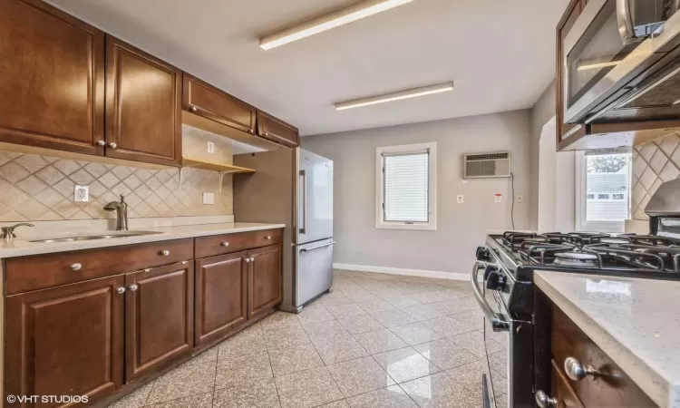 Kitchen featuring sink, tasteful backsplash, light stone counters, a wall mounted AC, and appliances with stainless steel finishes