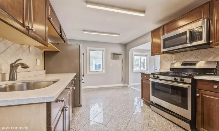 Kitchen featuring an AC wall unit, decorative backsplash, sink, and appliances with stainless steel finishes