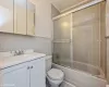 Full bathroom with vanity, backsplash, combined bath / shower with glass door, toilet, and tile walls