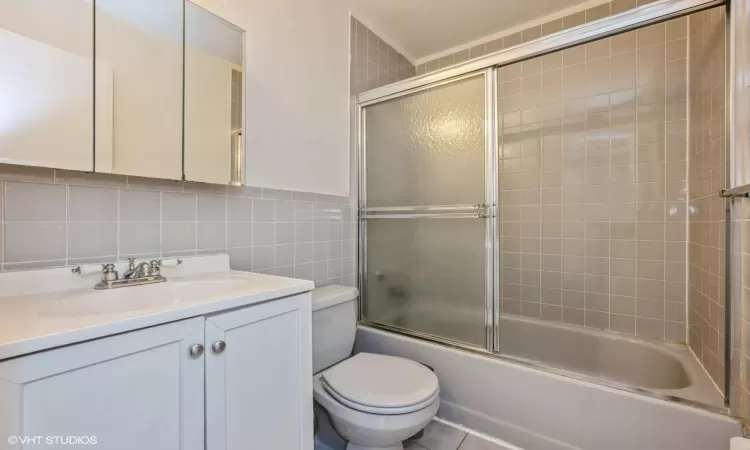 Full bathroom with vanity, backsplash, combined bath / shower with glass door, toilet, and tile walls