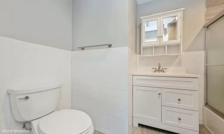 Full bathroom with vanity, bath / shower combo with glass door, tile walls, and toilet