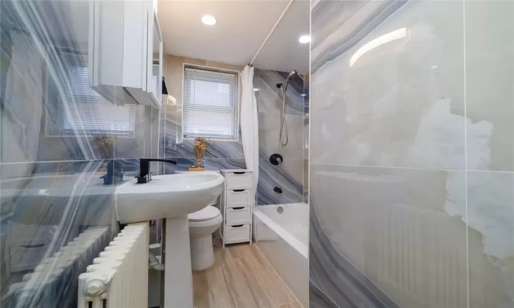 Bathroom featuring shower / bath combo, toilet, radiator heating unit, and tile walls