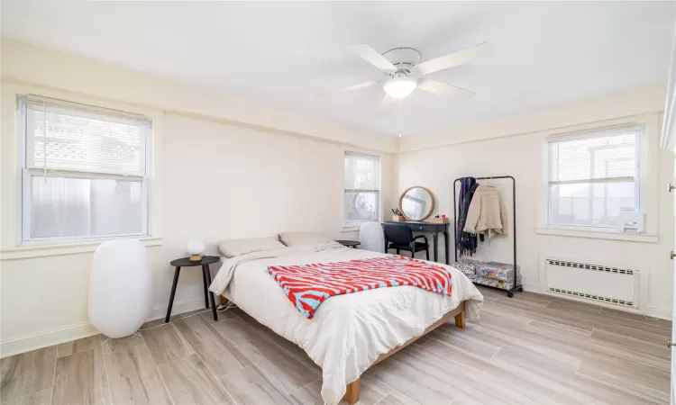 Bedroom featuring multiple windows, light hardwood / wood-style flooring, radiator, and ceiling fan