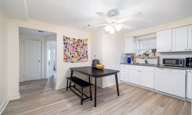 Kitchen with dishwasher, white cabinets, sink, dark stone countertops, and light wood-type flooring