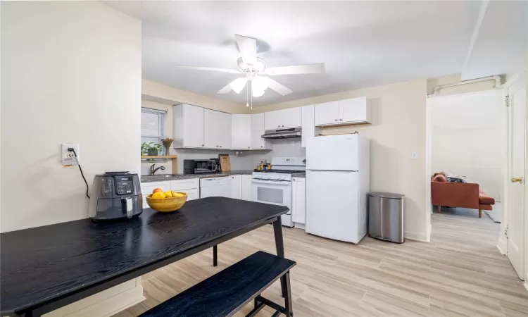 Kitchen with white appliances, ceiling fan, sink, white cabinets, and light hardwood / wood-style floors