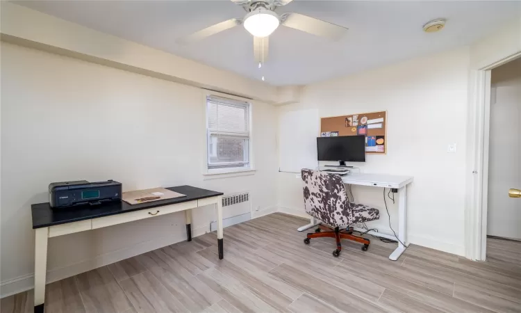 Office with ceiling fan, radiator heating unit, and light hardwood / wood-style floors