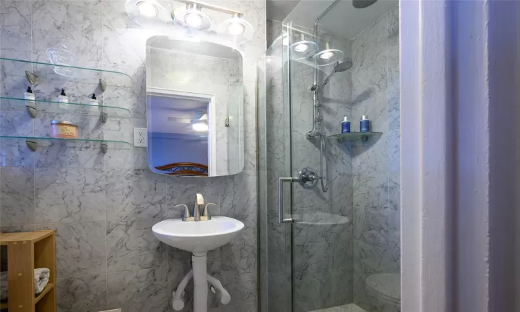 Bathroom with tile walls, a shower with shower door, and sink