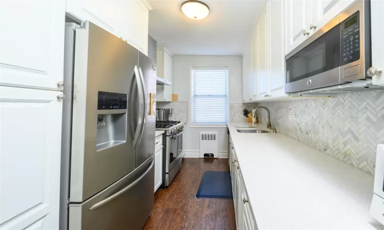 Kitchen with radiator, white cabinets, sink, dark hardwood / wood-style flooring, and stainless steel appliances