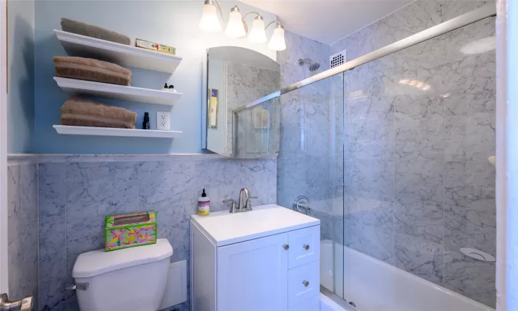 Full bathroom with vanity, toilet, tile walls, and enclosed tub / shower combo