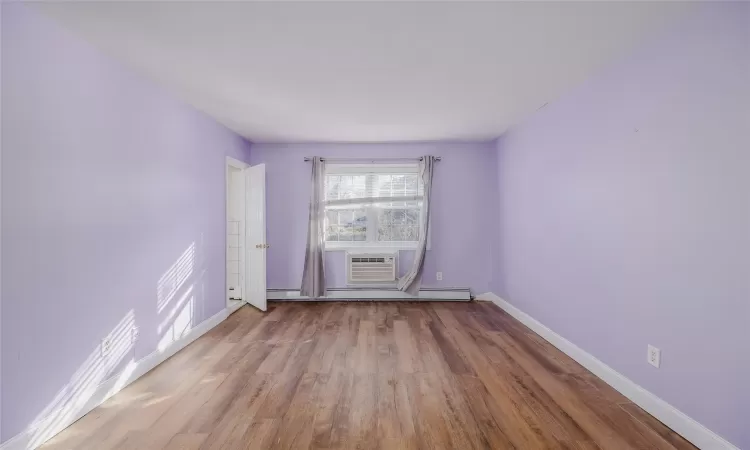 Empty room featuring light hardwood / wood-style floors, a wall unit AC, and a baseboard heating unit