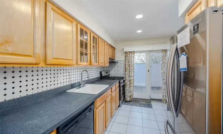 Kitchen featuring light tile patterned floors, sink, appliances with stainless steel finishes, and tasteful backsplash