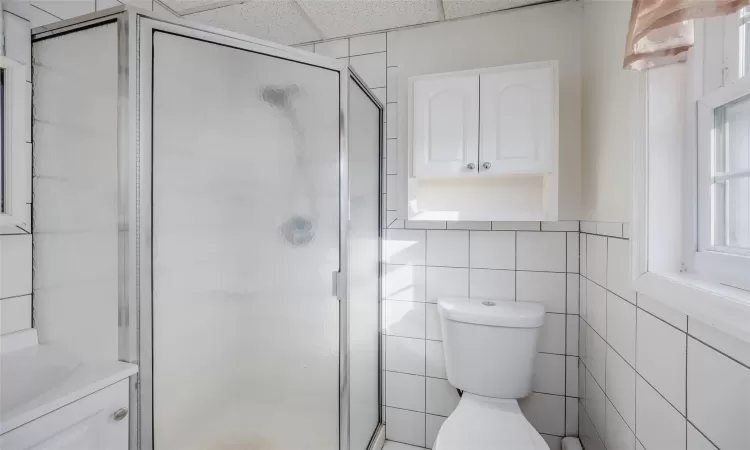 Bathroom featuring an enclosed shower, a paneled ceiling, toilet, and tile walls