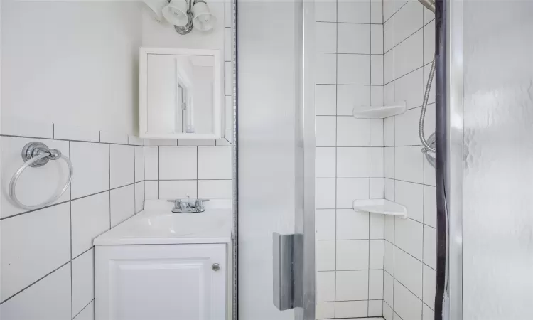 Bathroom featuring tiled shower, vanity, and tile walls