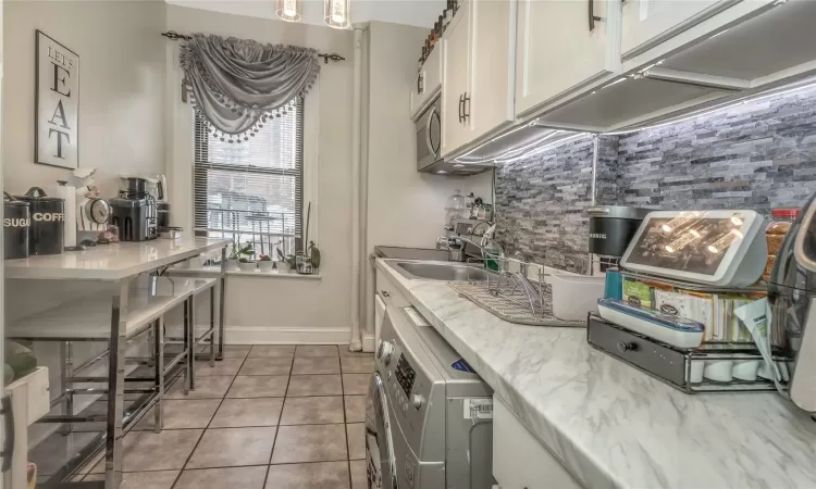 Kitchen with sink, tasteful backsplash, washer / dryer, white cabinetry, and stainless steel appliances