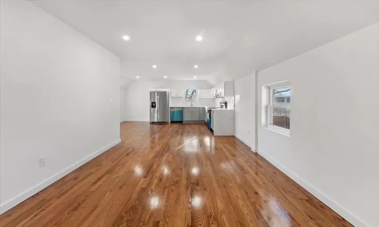 Unfurnished living room featuring sink, light hardwood / wood-style floors, and lofted ceiling