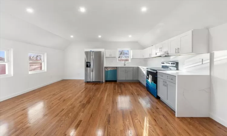 Kitchen with decorative backsplash, stainless steel appliances, vaulted ceiling, hardwood / wood-style flooring, and white cabinetry