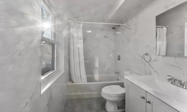 Full bathroom featuring shower / bath combo, vanity, tile walls, and toilet