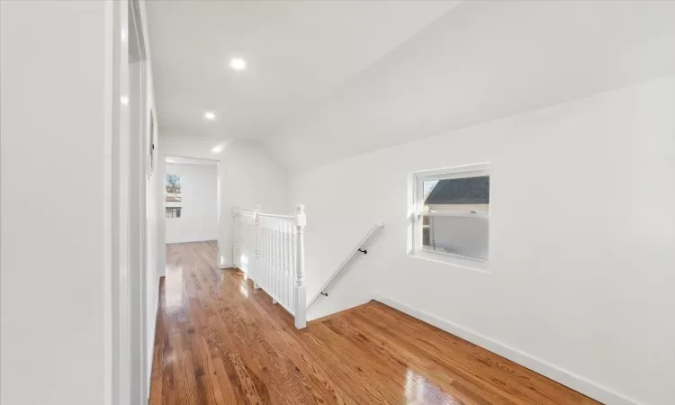 Hall with hardwood / wood-style flooring, a healthy amount of sunlight, and vaulted ceiling