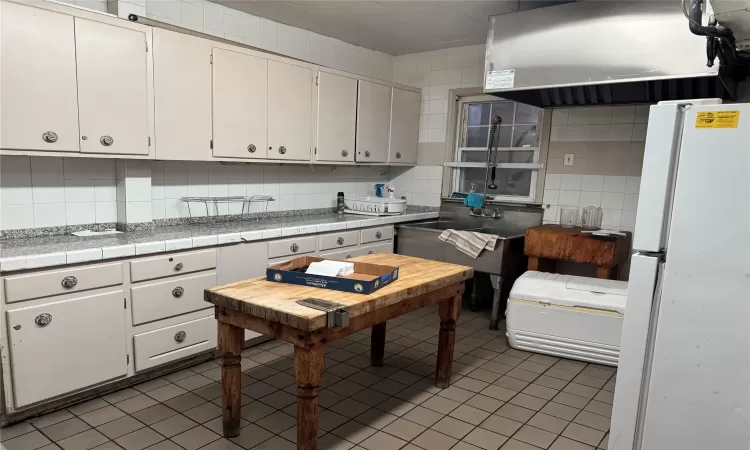 Kitchen with white refrigerator, tasteful backsplash, white cabinetry, and tile counters