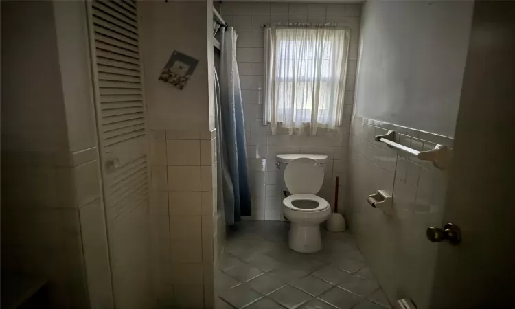 Bathroom with toilet, tile patterned floors, tile walls, and curtained shower