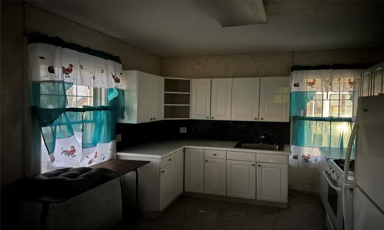 Kitchen featuring white appliances, backsplash, white cabinetry, and sink