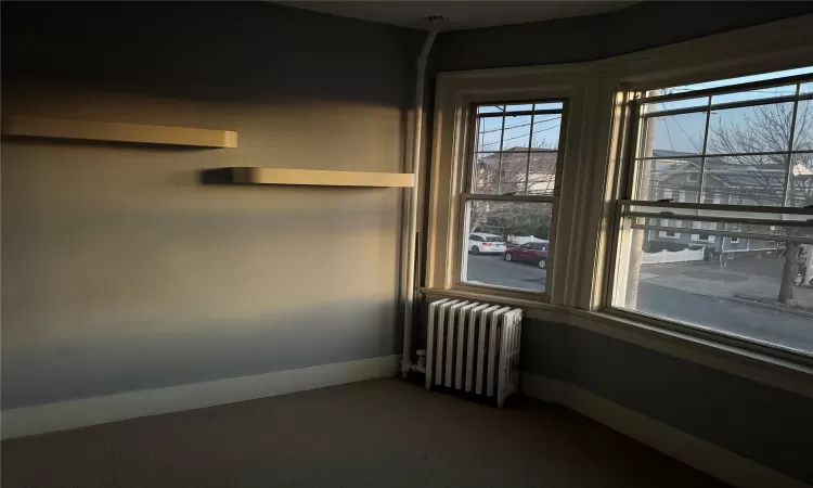 Unfurnished room featuring radiator and dark colored carpet