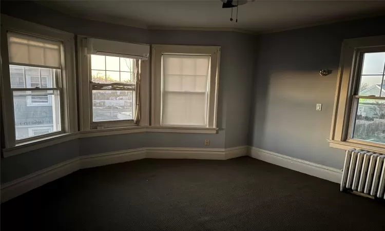 Carpeted empty room featuring an AC wall unit, crown molding, radiator heating unit, and ceiling fan