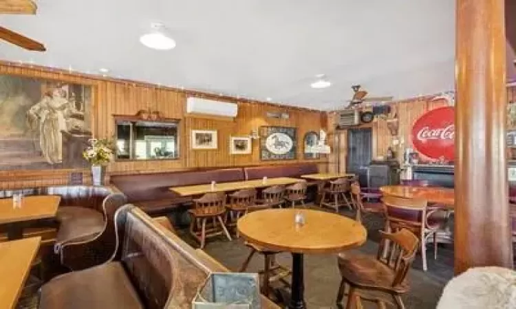 Carpeted dining room with a wall mounted air conditioner, ceiling fan, wood walls, and decorative columns