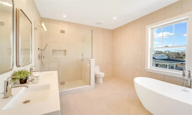 Full bathroom with toilet, tile patterned floors, tile walls, and independent shower and bath