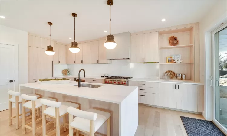 Kitchen with light brown cabinetry, a kitchen island with sink, sink, pendant lighting, and light hardwood / wood-style flooring