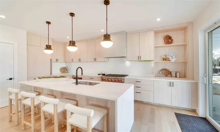 Kitchen featuring sink, light brown cabinets, light hardwood / wood-style flooring, decorative light fixtures, and a kitchen island with sink