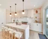 Kitchen with light brown cabinetry, sink, decorative light fixtures, light hardwood / wood-style flooring, and an island with sink