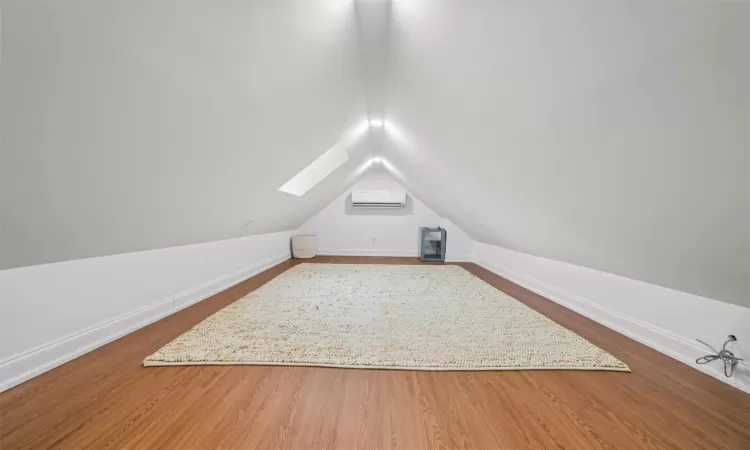 Bonus room with hardwood / wood-style floors, lofted ceiling with skylight, and a wall unit AC