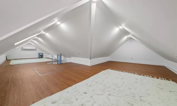 Additional living space with a wall mounted air conditioner, lofted ceiling, and wood-type flooring