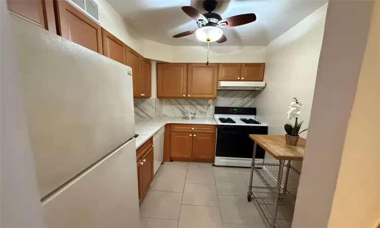 Kitchen with ceiling fan, white appliances, light tile patterned floors, and tasteful backsplash