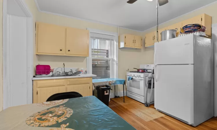 Kitchen with light wood-type flooring, light brown cabinetry, white appliances, and ornamental molding