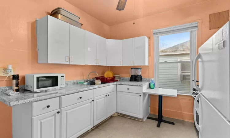 Kitchen featuring ceiling fan, sink, light stone counters, white appliances, and white cabinets