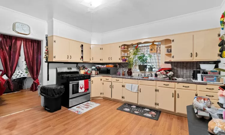 Kitchen featuring ornamental molding, stainless steel appliances, sink, cream cabinets, and light hardwood / wood-style flooring