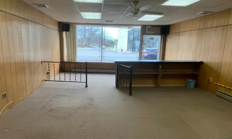 Miscellaneous room featuring baseboard heating, a paneled ceiling, wood walls, and light colored carpet