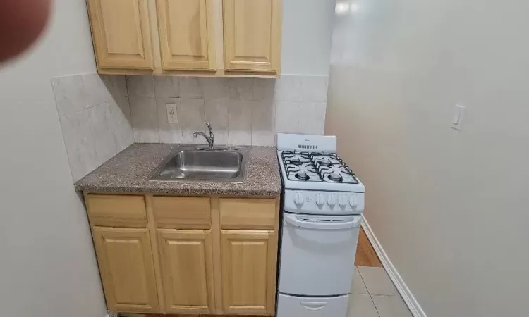 Kitchen featuring backsplash, light tile patterned flooring, sink, and white range with gas cooktop