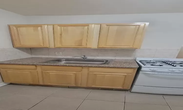 Kitchen featuring decorative backsplash, light brown cabinetry, white gas stove, and sink